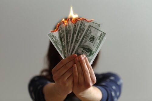 woman holding burning money in front of face